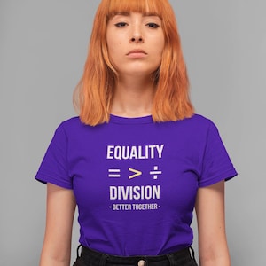 May include: A purple short-sleeved t-shirt featuring white text that reads EQUALITY, a mathematical symbol sequence of equals, greater than, and division, the word DIVISION, and the phrase - BETTER TOGETHER - in white text below.