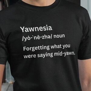 May include: Black t-shirt with the word "Yawnesia" and its phonetic pronunciation in white text. Below, the definition reads: "Forgetting what you were saying mid-yawn."
