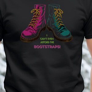 Puede incluir: Camiseta negra con un gráfico de dos botas militares, una magenta y otra turquesa, con cordones amarillos. El texto "I can't even afford the bootstraps!" está debajo de las botas.