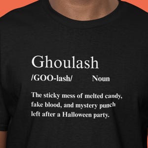 May include: Black t-shirt with the word "Ghoulash" in white, along with a definition describing the aftermath of a Halloween party. The definition includes "melted candy, fake blood, and mystery punch."