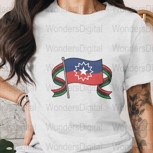 Puede incluir: Una camiseta gris claro con un diseño gráfico de la bandera de Juneteenth. El diseño de la bandera incluye una parte superior azul, una inferior roja, una estrella blanca y una cinta en rojo, negro y verde. La camiseta tiene mangas cortas.