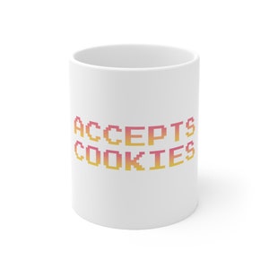 Pode incluir: Caneca de cerâmica branca com o texto "ACCEPTS COOKIES" em uma fonte pixelada com um degradê de rosa e amarelo.
