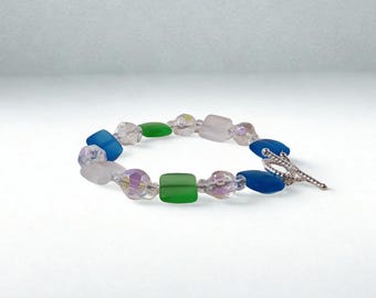 May include: A beaded bracelet featuring a variety of colorful beads. The bracelet includes blue, green, clear, and iridescent beads. The clasp is silver-colored. The bracelet is approximately 7 inches in length.