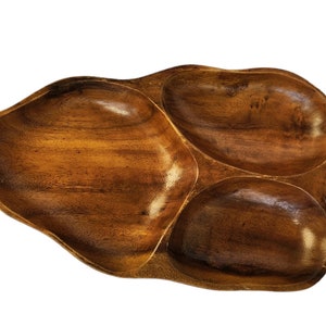 May include: A wooden serving tray shaped like a leaf with three separate compartments. The tray is made of dark brown wood and has a smooth, polished finish.