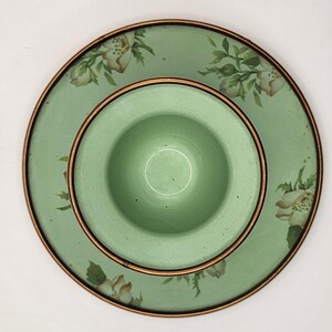 Puede incluir: Un juego de platos de cer&aacute;mica verde claro con un dise&ntilde;o floral. El juego incluye un cuenco peque&ntilde;o y centrado y un plato m&aacute;s grande, ambos con un borde color cobre. El plato presenta un patr&oacute;n de flores blancas y beige con hojas verdes.