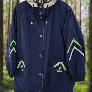 May include: A navy blue jacket with a hood, featuring gold buttons and green and white chevron accents on the sleeves. The jacket has two front pockets with green and gold details. It is hanging on a wooden hanger.