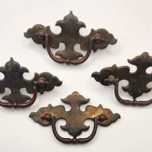 May include: Four antique cabinet pulls with a distressed, green and copper finish. Each pull has a decorative, ornate design and a D-shaped handle.