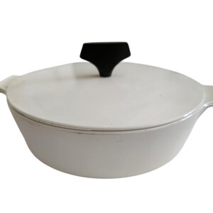 May include: White cast iron Dutch oven with a black handle on the lid. The pot has two side handles and a rounded shape. A classic piece for cooking soups, stews, and baking bread.