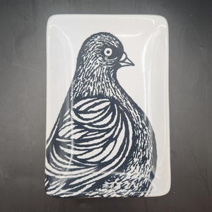 May include: A rectangular white ceramic tray featuring a black graphic illustration of a bird in profile. The bird design displays detailed line work on its feathers and body. The word CARNEY is printed in small black letters at the bottom right.