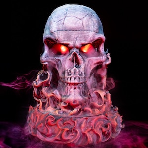 May include: A three-dimensional skull sculpture with a weathered gray finish and glowing red eyes. The base of the skull is surrounded by sculpted, flame-like textures that are illuminated in shades of red and orange, with wisps of red smoke.