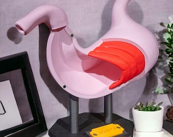 May include: An anatomical model of a human stomach featuring a light pink exterior and a bright orange interior section. The model is mounted on two gray cylindrical supports attached to a black hexagonal base with a small yellow rectangular plaque.
