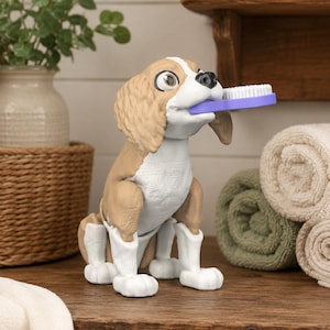 Puede incluir: Una figura de perro de color canela y blanco con grandes ojos marrones, sentada en posición vertical. El perro tiene patas blancas y sostiene un cepillo de dientes morado con cerdas blancas horizontalmente en la boca como accesorio de baño.