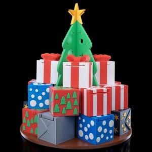 K&ouml;nnte beinhalten: Ein dekoratives Display mit einem gr&uuml;nen Kunststoff-Weihnachtsbaum, der von einem gelben Stern gekr&ouml;nt wird, umgeben von einem Stapel quadratischer Geschenkboxen. Die Boxen sind mit rot-wei&szlig;en Streifen, blauen Punkten, gr&uuml;nen Tannen und grau verziert.