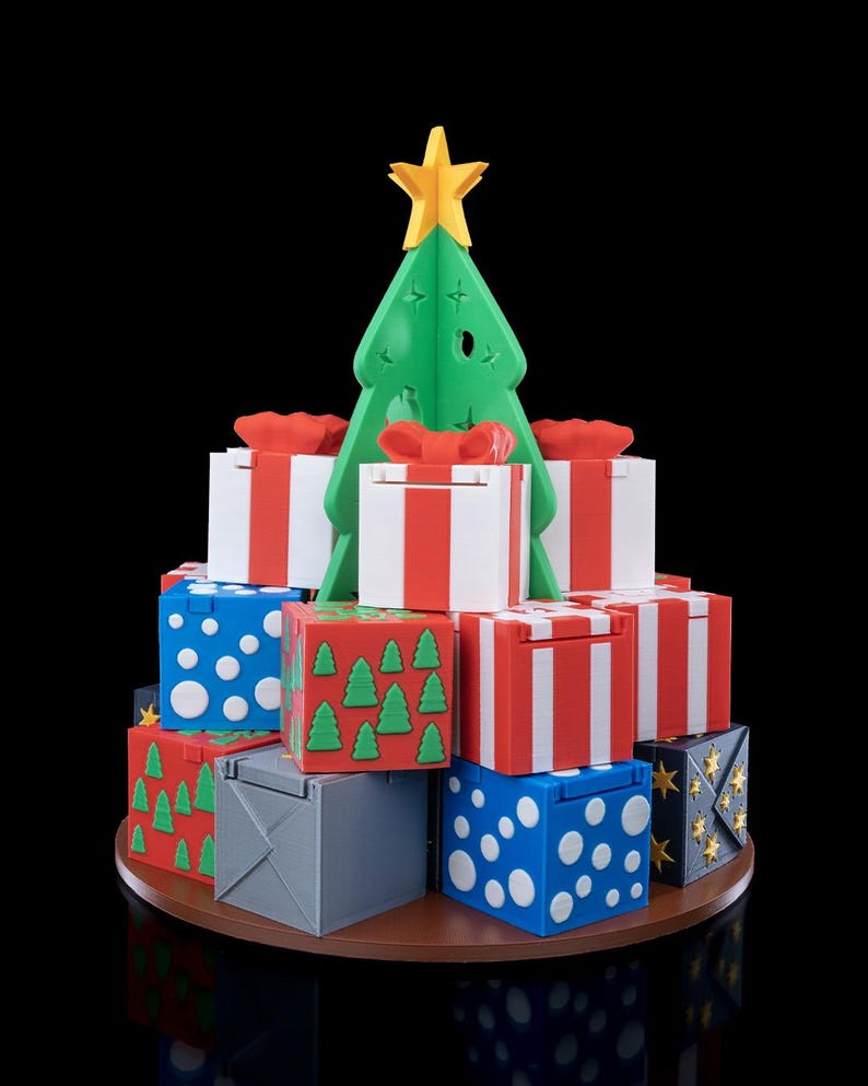 K&ouml;nnte beinhalten: Ein dekoratives Display mit einem gr&uuml;nen Kunststoff-Weihnachtsbaum, der von einem gelben Stern gekr&ouml;nt wird, umgeben von einem Stapel quadratischer Geschenkboxen. Die Boxen sind mit rot-wei&szlig;en Streifen, blauen Punkten, gr&uuml;nen Tannen und grau verziert.
