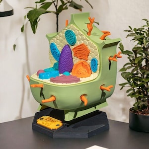 May include: A 3D-printed model of a plant cell featuring a light green exterior, a textured cream-colored interior, and various colorful organelle inserts in purple, orange, and blue. The model sits on a black hexagonal base with a gold-colored plaque.