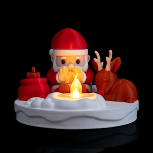 Könnte beinhalten: Weihnachtsdekoration mit einem Weihnachtsmann in rotem Anzug und Mütze, Händen an einer Kerze. Ein braunes Rentier ist daneben. Der weiße Sockel ist mit einem Schneemuster und einer roten Geschenktüte verziert.