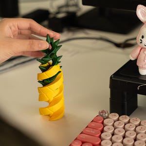 May include: A yellow and green pineapple-shaped toy made of plastic. The toy is made up of several pieces that can be stacked on top of each other.