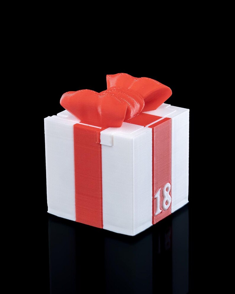 K&ouml;nnte beinhalten: Eine wei&szlig;e, w&uuml;rfelf&ouml;rmige Geschenkbox mit einem roten Schleifendesign an den Seiten und einer roten Schleife oben. Auf der Vorderseite ist die Zahl 18 in Wei&szlig; eingepr&auml;gt. Das Objekt weist eine sichtbare 3D-Druckstruktur auf der Oberfl&auml;che auf.