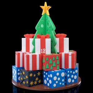 May include: A 3D-printed Christmas tree topper in yellow, centered above a tiered arrangement of square gift boxes. The boxes feature red and white stripes, blue with white polka dots, or black with gold stars. One box displays the number 12.
