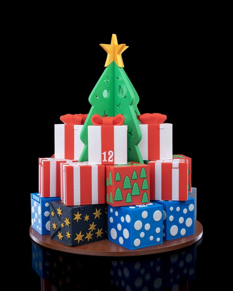 K&ouml;nnte beinhalten: Ein 3D-gedruckter Weihnachtsbaumaufsatz in Gelb, platziert &uuml;ber einer gestuften Anordnung quadratischer Geschenkboxen. Die Boxen sind mit rot-wei&szlig;en Streifen, blauen Punkten auf wei&szlig;em Grund oder goldenen Sternen auf schwarzem Grund verziert.