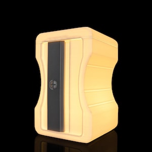 May include: A light-colored, rectangular pencil sharpener-shaped object with a smooth, matte finish. It features a central, vertical dark gray panel with a circular screw head in the middle, set against a soft, warm, glowing light-toned body.