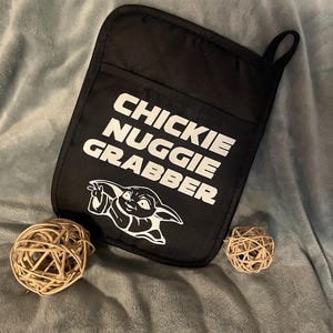 May include: Black oven mitt with a white graphic of a baby Yoda character and the text "Chickie Nugglie Grabber".