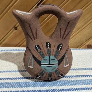 Könnte beinhalten: Eine handbemalte Keramikvase im indianischen Stil mit traditionellem Design. Die Vase hat einen runden Körper mit einem Henkel und zwei Öffnungen oben.