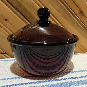 Puede incluir: Un platito de caramelo de vidrio vintage con tapa. El plato está hecho de vidrio rojo oscuro con un pomo negro en la tapa. El plato tiene un patrón de remolino.