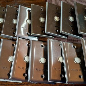 May include: A collection of rectangular, brushed metal call buttons arranged in two rows. Each unit features a central circular button and the text "PRESS TO CALL" engraved on the lower portion of the metallic faceplate, with screw holes at the top and bottom.