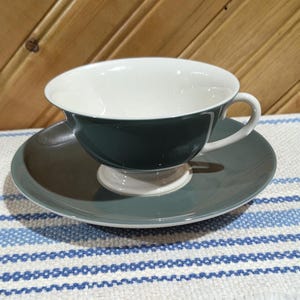 Puede incluir: Un juego de taza y platillo de té verde con interior blanco. La taza tiene una forma redondeada y un asa. El platillo es una forma redonda simple.