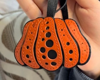 May include: Orange leather pumpkin charm with black stitching and holes. The charm has a black leather loop for hanging.
