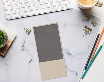 May include: A top-down view of a workspace with a white keyboard, a cup of coffee, and a notepad. The notepad is rectangular with a gray top and a beige bottom. Gold binder clips and colored pencils are also present.