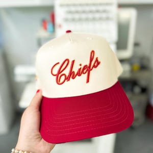 May include: A white and red baseball cap with the word "Chiefs" embroidered in red on the front.