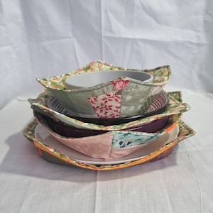 May include: A stack of four bowl cosies made from patchwork fabric with floral patterns in shades of green, pink, and white. The cosies are designed to protect bowls from heat and scratches.