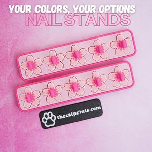 May include: Two pink nail stands with flower-shaped holders. Each stand has five flower designs. The text "YOUR COLORS, YOUR OPTIONS NAIL STANDS" is at the top. A black rectangle with "thecatprints.com" is at the bottom.