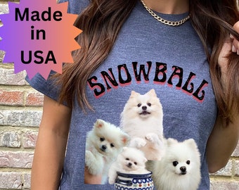 May include: A navy blue t-shirt with the word "SNOWBALL" in red and black above four fluffy white Pomeranian dogs. The shirt also has a "Made in USA" graphic.