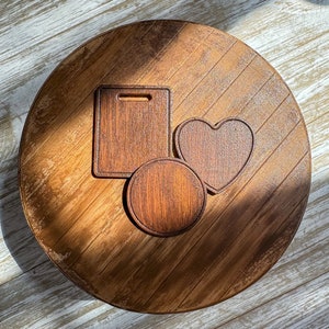 May include: Three wooden cutting boards in different shapes: a rectangle, a heart, and a circle. The boards are arranged on a brown wooden surface.