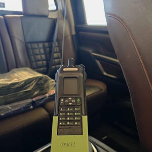 May include: A black Baofeng DM32 handheld two-way radio with a long antenna, a digital display, and a numeric keypad. The lower portion of the device is encased in a light green protective cover with the text DM32 printed in a dark script font.