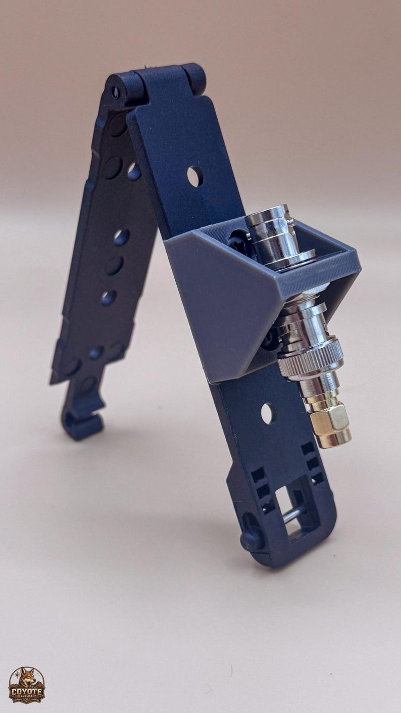 May include: A dark blue, hinged, multi-hole mounting strap with a grey, 3D-printed, triangular bracket attached. A metallic BNC connector is secured within the bracket, featuring a silver-toned cylindrical body and a gold-toned threaded base.