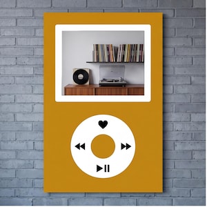 May include: A mustard yellow rectangular wall art piece featuring a white digital music player interface with a circular control wheel. The screen displays a photograph of a record player, a vinyl record, and a shelf filled with vinyl records.