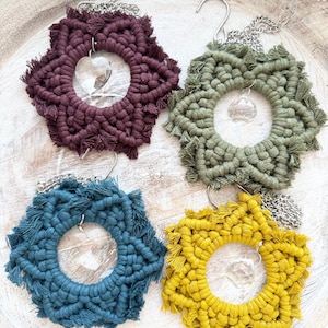 May include: Four macrame star-shaped wall hangings with crystal accents. The hangings are in shades of burgundy, green, blue, and yellow.