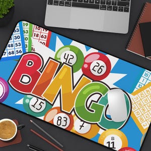May include: A rectangular mousepad with a colorful bingo theme. The design features the word "BINGO" in large, multi-colored letters, surrounded by bingo balls and numbers. A computer mouse rests on the pad, with a blue background.