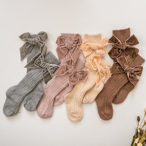May include: Five pairs of knee-high socks with velvet bows in different colors. The socks are ribbed and come in gray, pink, beige, brown, and a darker brown.