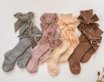 Peut inclure: Cinq paires de chaussettes hautes avec des nœuds en velours de différentes couleurs. Les chaussettes sont côtelées et disponibles en gris, rose, beige, marron et marron foncé.