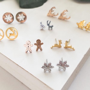 Könnte beinhalten: Sortiment an Weihnachtsohrringen in Gold, Silber und Roségold. Die Ohrringe zeigen Motive von Schneeflocken, Rentieren, Weihnachtsbäumen und Lebkuchenmännern.