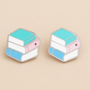 Peut inclure: Deux épingles en émail en forme de piles de livres. Chaque épingle représente une pile de trois livres bleus, blancs et roses, avec un livre supérieur turquoise. Un petit cœur rouge est sur le livre rose. Les épingles ont un contour argenté.