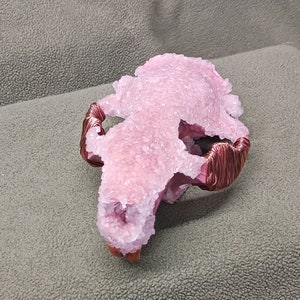 May include: A pink crystal skull with copper wire wrapped around the jawline. The skull is covered in small crystals.