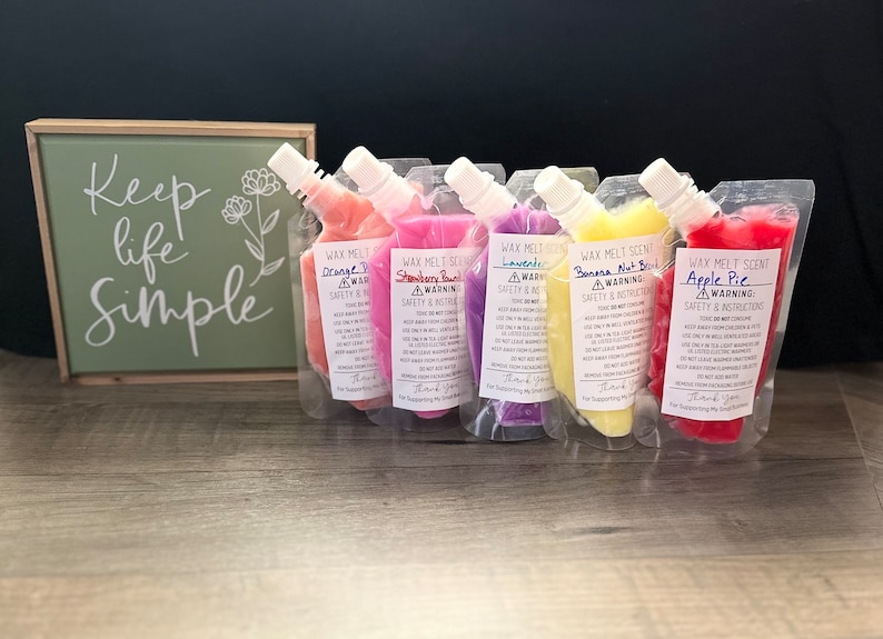 K&ouml;nnte beinhalten: F&uuml;nf Beutel mit Wachs-Schmelzduft in verschiedenen Farben, darunter Pink, Rot, Gelb, Lila und Orange. Jeder Beutel ist mit einem Etikett mit dem Duftnamen und Sicherheitshinweisen versehen. Die D&uuml;fte sind Orange, Erdbeer-Explosion, Lavendel, Bananen-Nussbrot und Apfelkuchen.