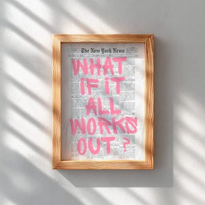 Puede incluir: Una impresi&oacute;n enmarcada que muestra una p&aacute;gina de peri&oacute;dico antigua con el texto WHAT IF IT ALL WORKS OUT? escrito en letras grandes, negritas y de color rosa brillante en el centro. El marco es de madera clara con veta visible.