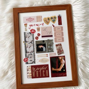 Op de afbeelding: Een ingelijste collage met een bruine houten lijst. De collage bevat foto's, lucifersdoosjes en stickers met zinnen als "you + me = ♡" en "I Love You". Het thema lijkt romantisch te zijn.